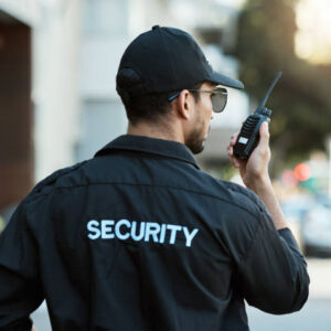 Radio, man and a security guard or safety officer outdoor on a city road for communication. Back of a person with a walkie talkie on urban street to report crime for investigation and surveillance